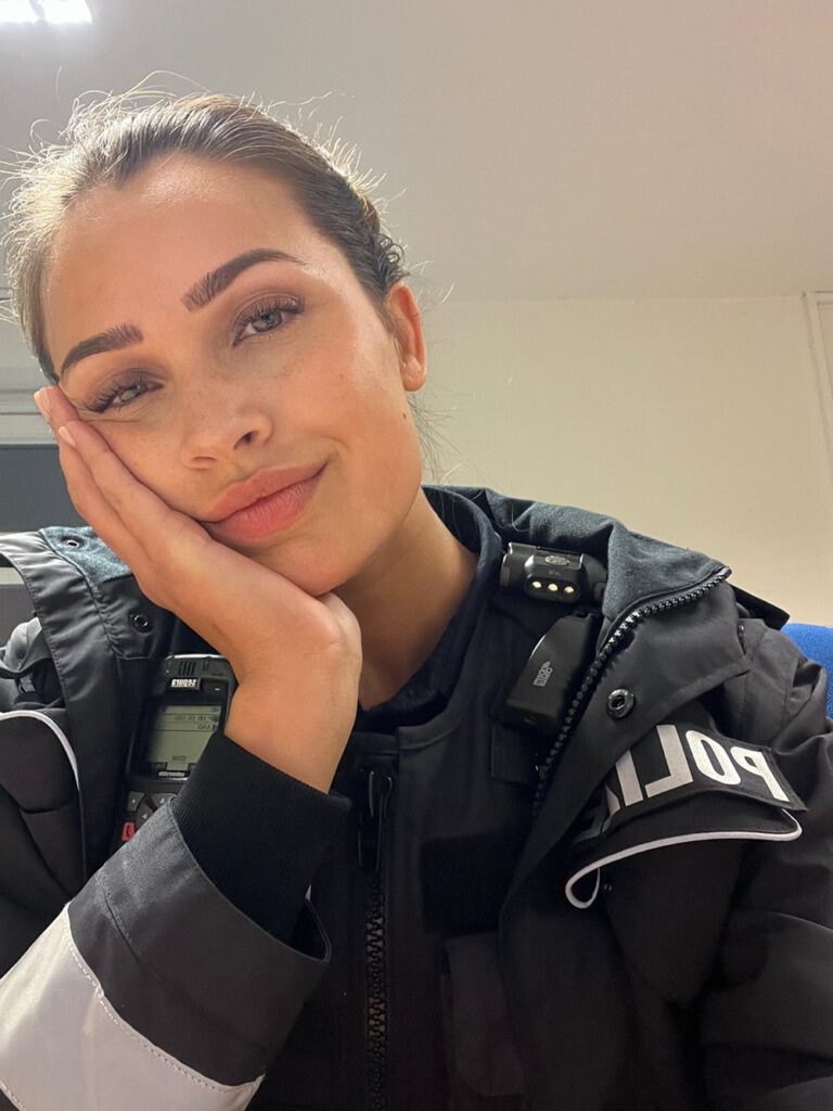Porträt von Lena Westermann in Polizeijacke mit Funkgerät, Hand stützt ihr Gesicht, entspannter Blick.