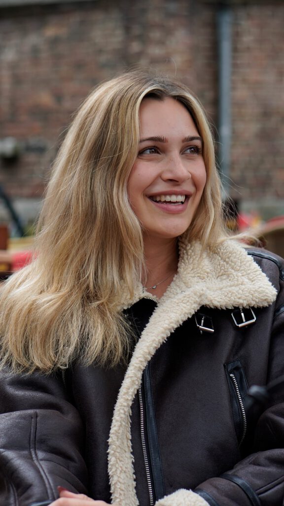 Porträt von Lena Westermann im braunen Lederjacke mit Fellkragen, lachend im Freien.