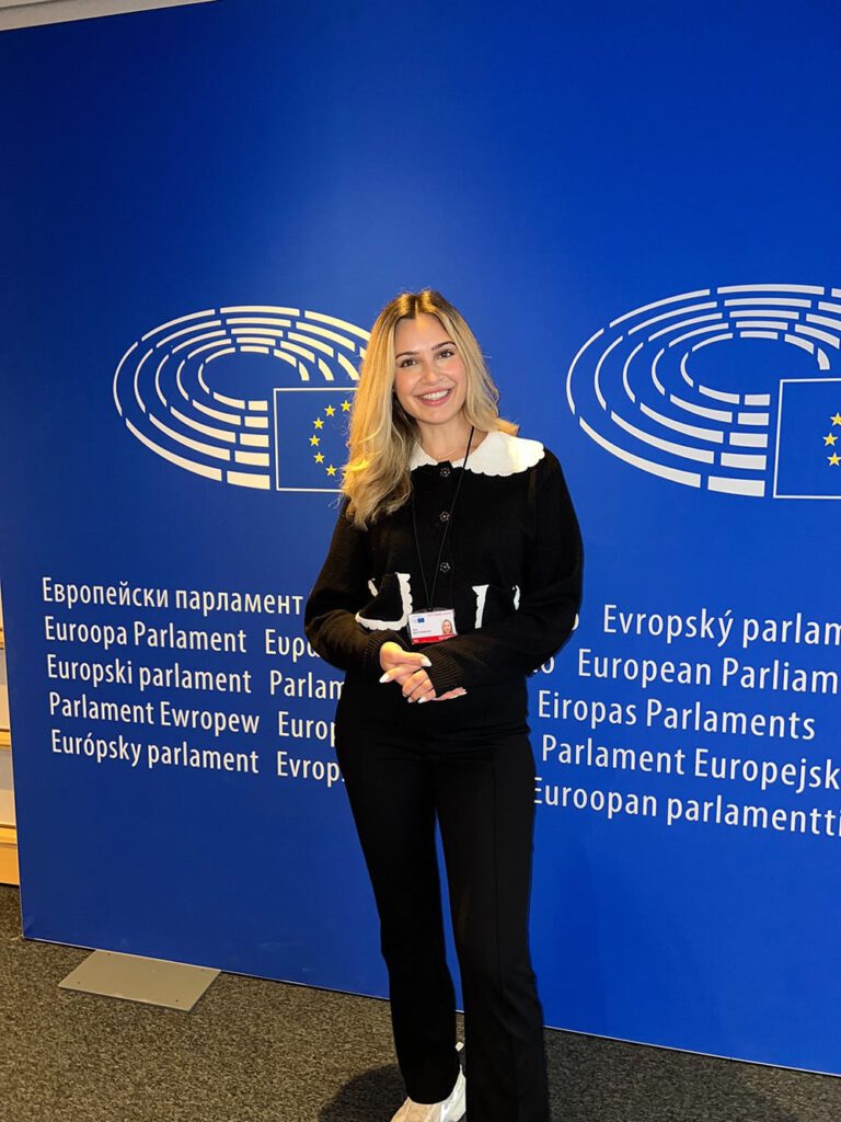Lena Westermann steht im Europäischen Parlament vor blauem Hintergrund mit EU-Logo, lächelnd in die Kamera.