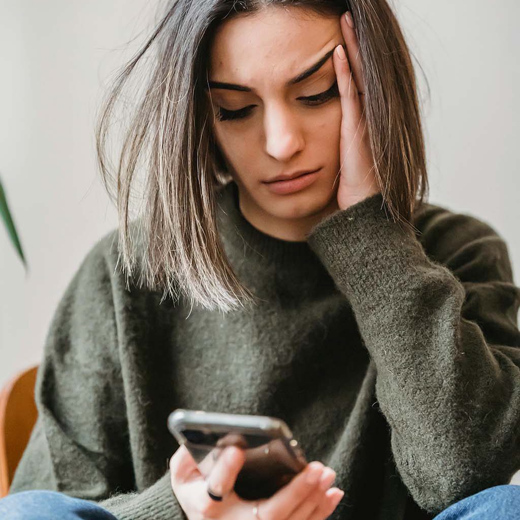 Foto einer unglücklichen jungen Influencerin, die auf ein Smartphone starrt