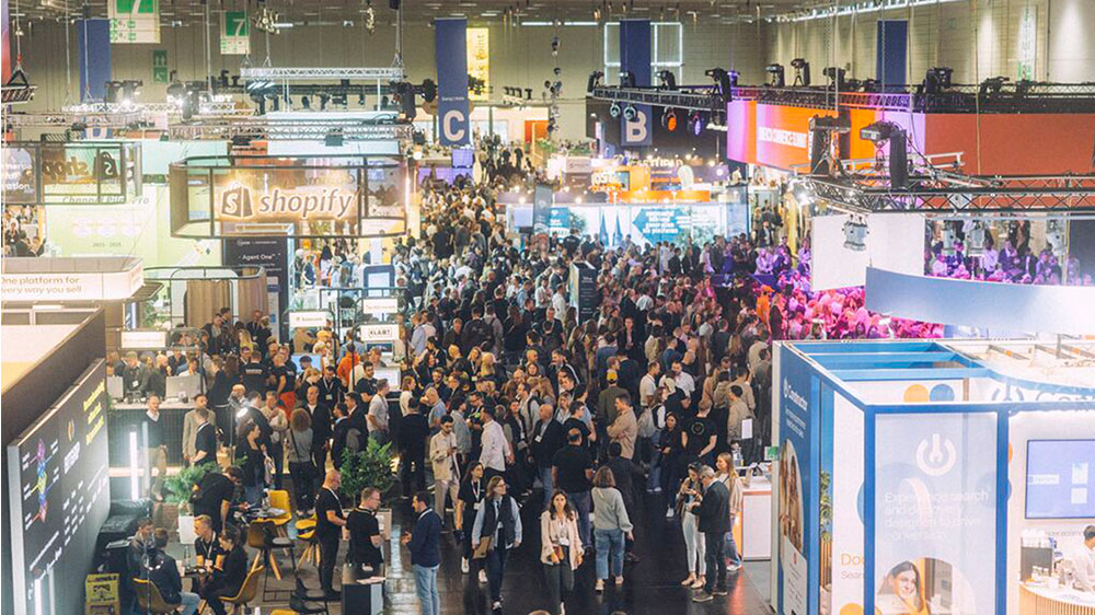 Alt-Text: Volle Messehalle auf der DMEXCO mit Ständen und Besuchern, Branchen-Event für Digital Marketing, Commerce und Technologie