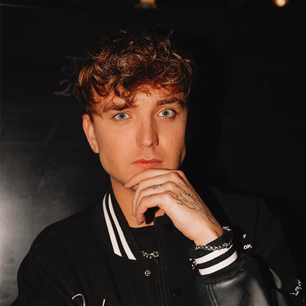 Porträt von Jonas Wuttke mit nachdenklichem Blick, Hand am Kinn, dunkler Hintergrund.