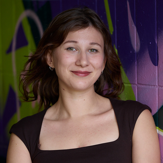 Leonie Ida steht vor einer farbigen Wand, Porträtaufnahme mit urbanem Hintergrund